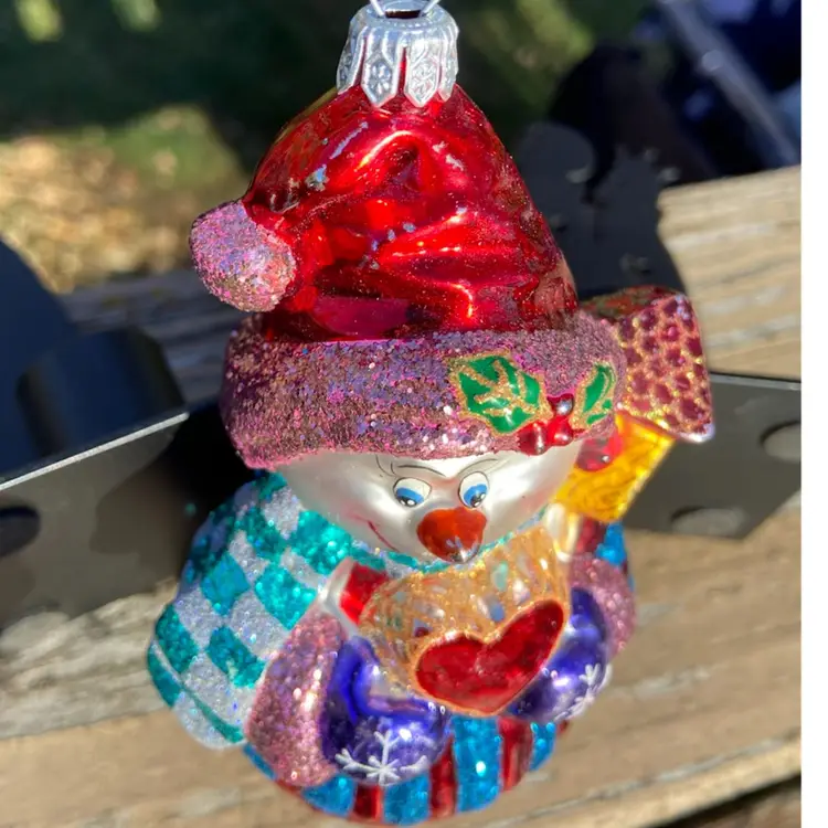 Blown Glass Snowman Christmas Ornament. Purple Mittens Holding Red Heart With Gift On Shoulder. Red Hat & Green And Silver Checkered Scarf. Attached Hanger. 5.5”h x 3”w.