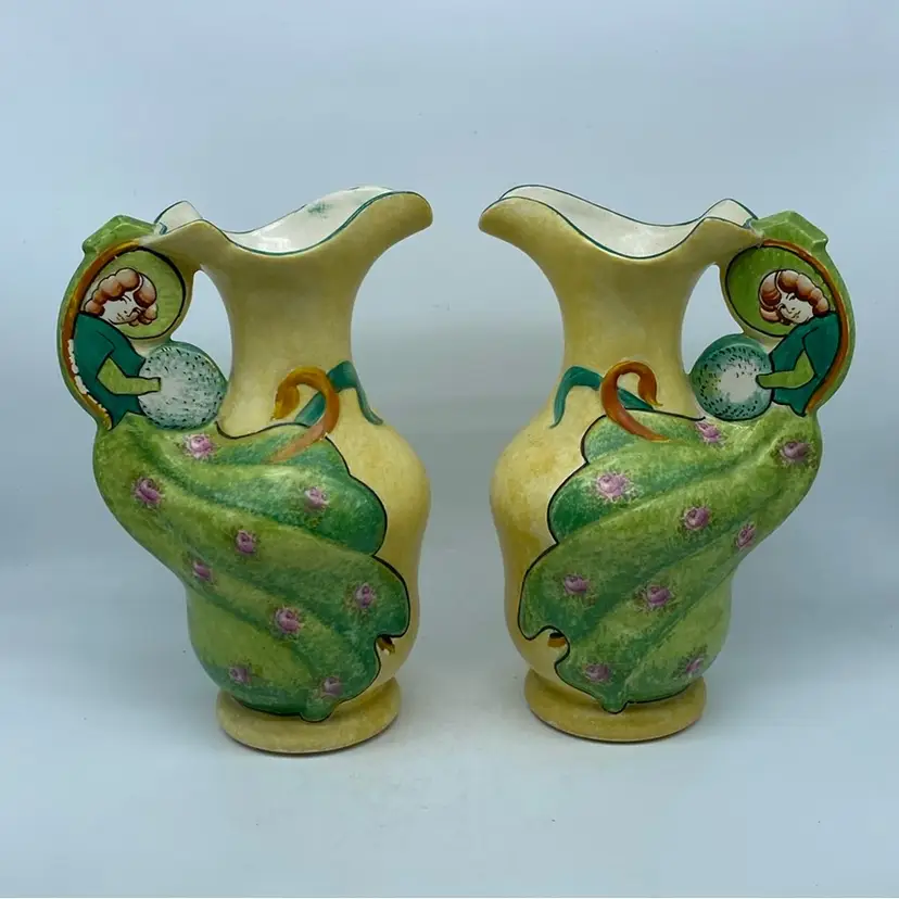 #2105 A pair of Art Nouveau ceramic pitchers manufactured by Royal Art Pottery of Longton, England, featuring hand-painted Girl Holding A Hand Warmer and Wearing floral Dress design 10 “ x 5”