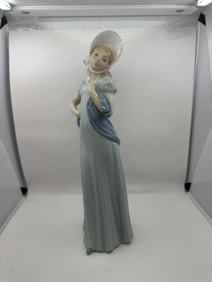 A Nao Lladro porcelain figurine of a lady with a bonnet and scarf, 13”