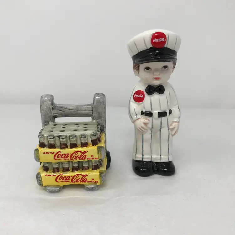 Coca Cola delivery man and cart salt and pepper shakers. 1995. Original Coca Cola stickers, stoppers. Vintage advertising. Man 3.75 H x 1.25 L x 1.25 W; cart 2 H x 2 L x 1.5 D.
