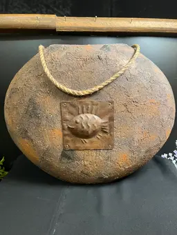SEE PICS!!  Pottery Free Standing Vase-Decorative Accent. Maybe Made of Clay? Has Textured, Rustic Finish & Appears Weathered. It is Round, Flattened Shape w/ Rope Handle and a Central Metal Medallion w/ Fish Motif on Both Sides