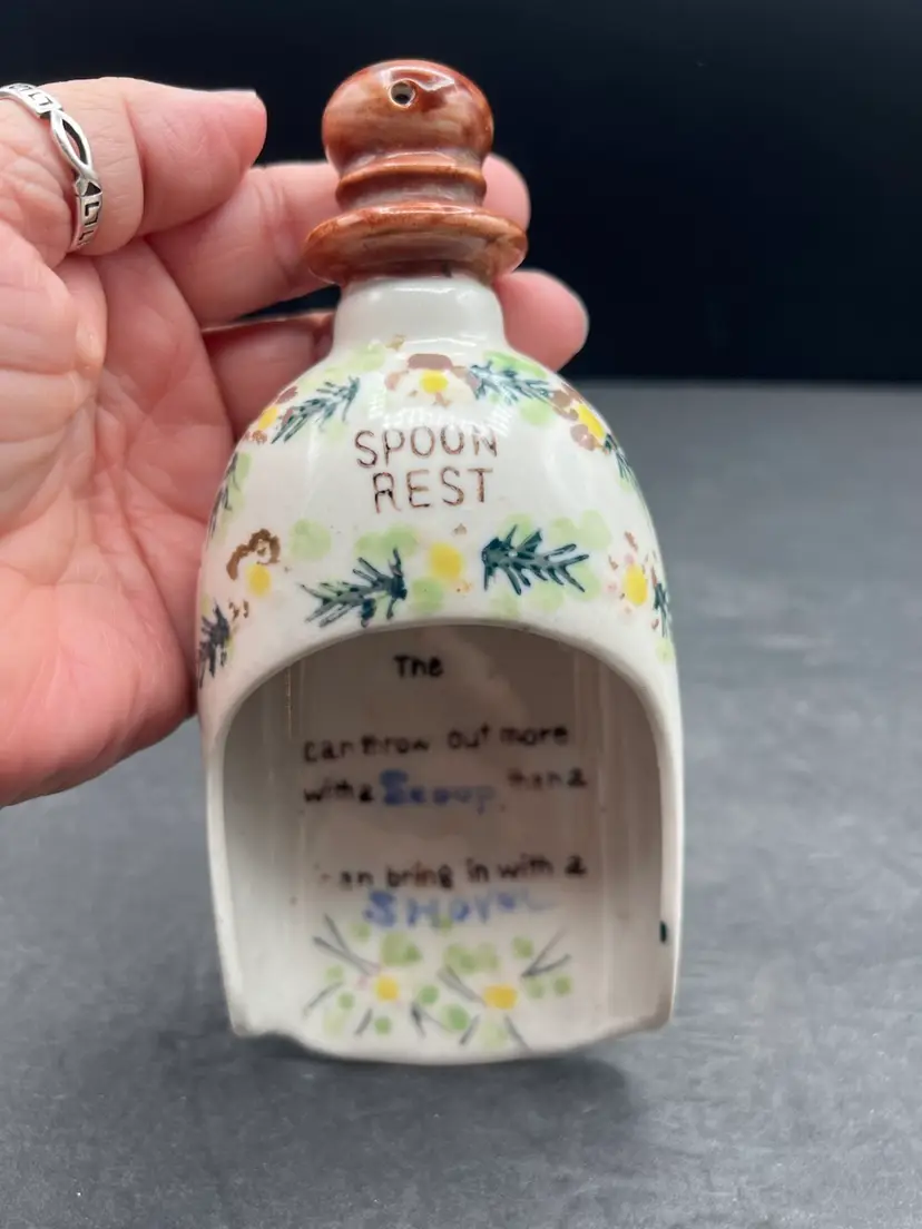 #575B Vintage Scoop Shaped Ceramic Wall Hanging Spoon Rest. Hand Painted With Partial Phrase ‘The Wife Can Throw Out More With A Scoop Than The Husband Can Throw Out With A Shovel’