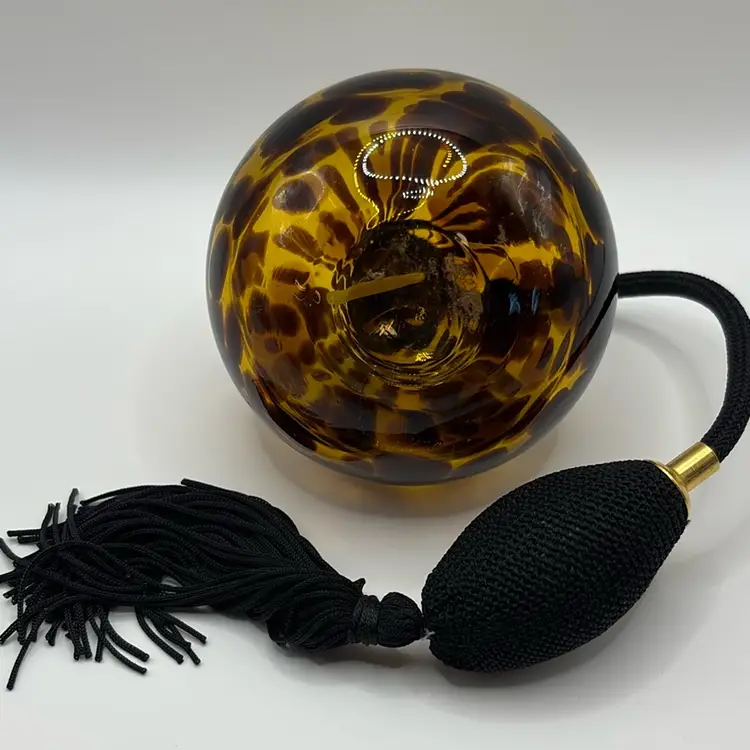 hand-blown glass perfume atomizer featuring a tortoise shell or leopard print pattern. Amber colored glass with dark brown spot patterns. 
Equipped with a gold-tone metal atomizer collar and a black squeeze bulb sprayer.