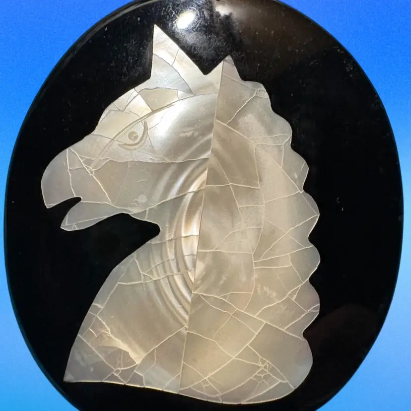 Vintage mother-of-pearl inlay horse head pendant on black background.
