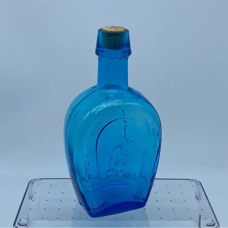 #0230 Decorative blue glass bottle with a horseshoe motif made in Taiwan 7” x 3” Flaw