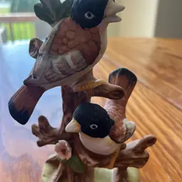 A hand-painted ceramic figurine of two birds on a branch. 7.5” Tall
