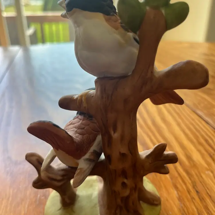 A hand-painted ceramic figurine of two birds on a branch. 7.5” Tall