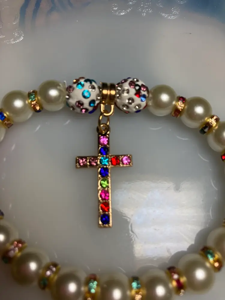 Cross and Faux Pearl Bracelet.
Multicolored Crystal Spacer Beads.
Multicolored Crystals in The Cross.
Gold Toned Accents. 
Stretch