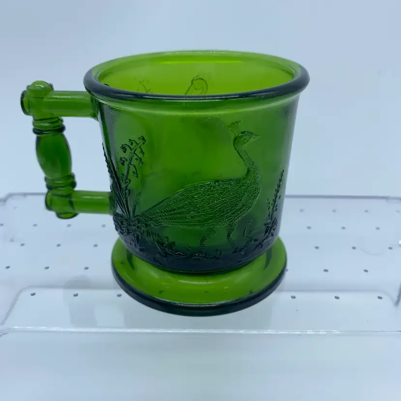 #0311 A green pressed glass mug by Degenhart featuring peacock and stork motifs.