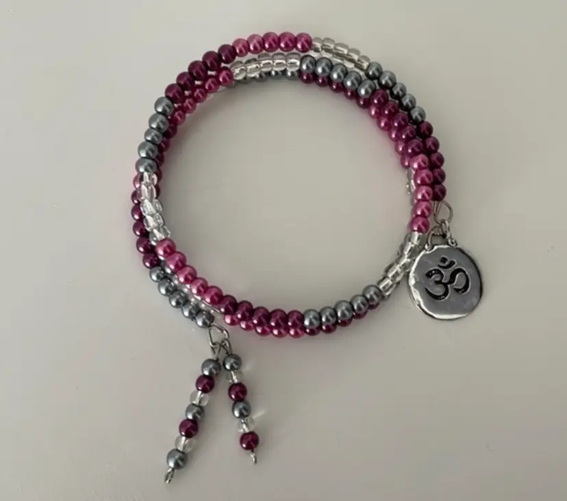 New, handmade wrap bracelet in purple and silver with Om “the sound of the universe” charm, approx. 2.5” in diameter. White drawstring storage bag included.