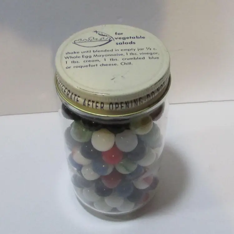 lot of vintage glass marbles in glass jar with vegetable salad recipe top