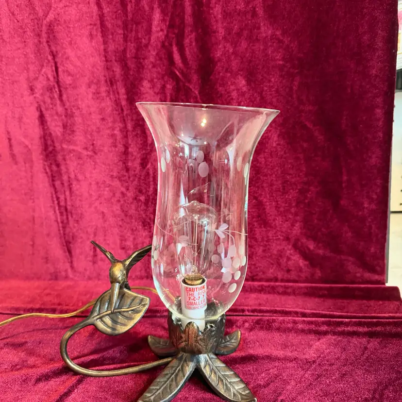A Stunning vintage brass electric lamp featuring a hummingbird and leaf base with a glass hurricane shade.