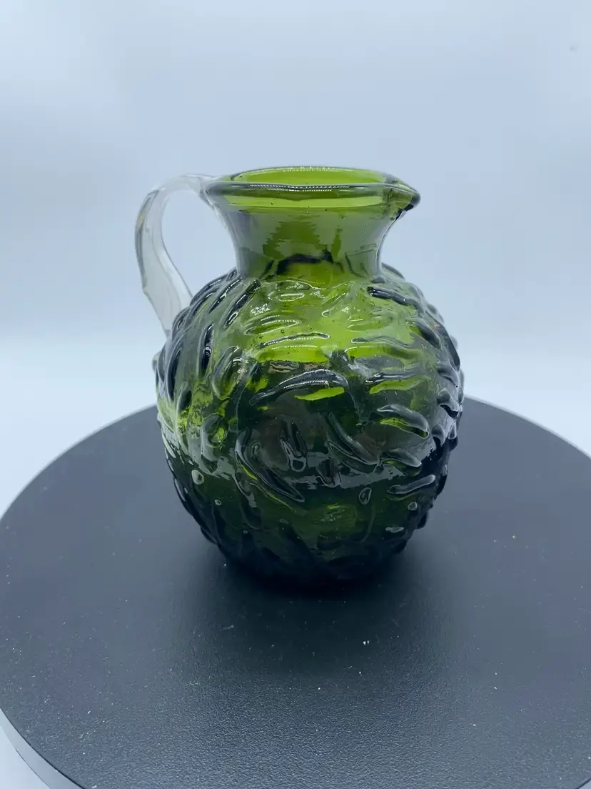 #0323 Vintage emerald green glass pitcher with applied clear handle and textured pattern.