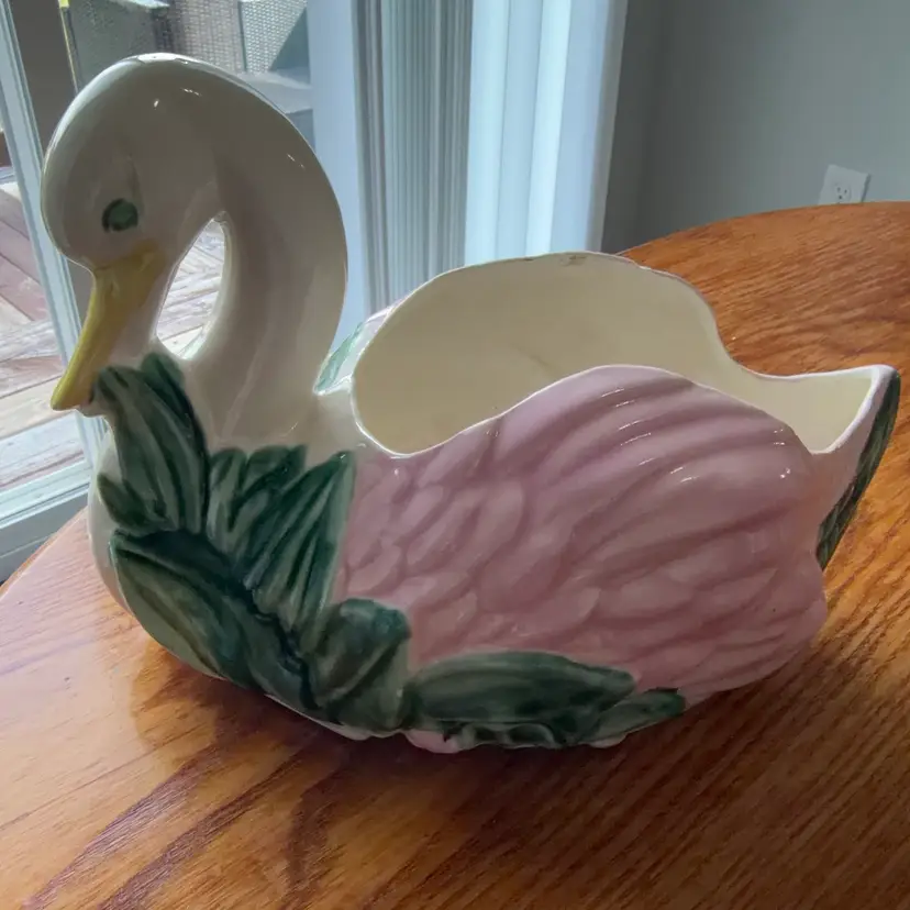A vintage ceramic swan planter with pink wings and green foliage.13x8.5”