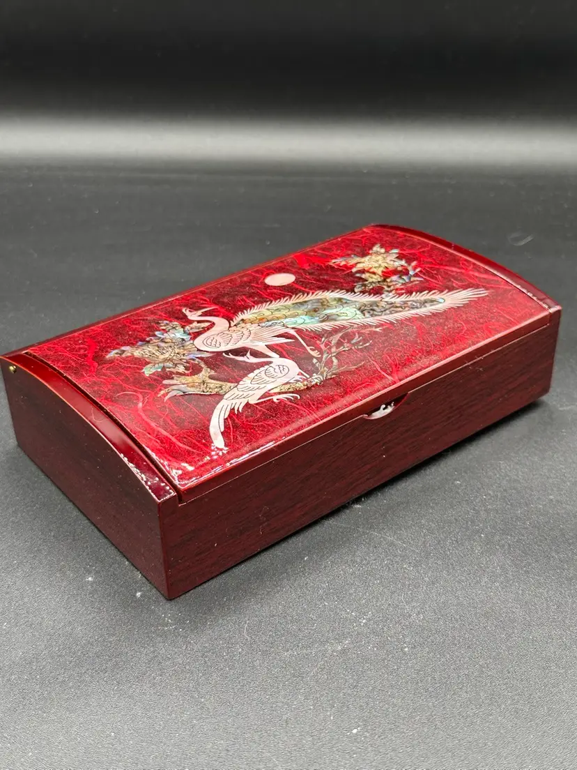lacquered wooden jewelry box with a mother-of-pearl inlay. The inlay features two cranes, which are a symbol of happiness and longevity in many Asian cultures