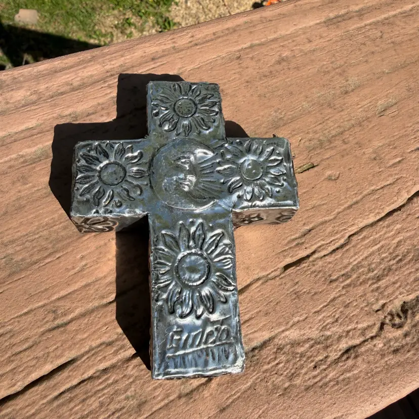 Mexican folk art milagro cross, handcrafted from embossed metal and featuring floral designs and a central sun face