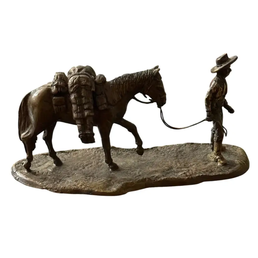 bronze sculpture depicts a cowboy leading a packed horse, similar in style to works by artists like Nancy R. Jellico