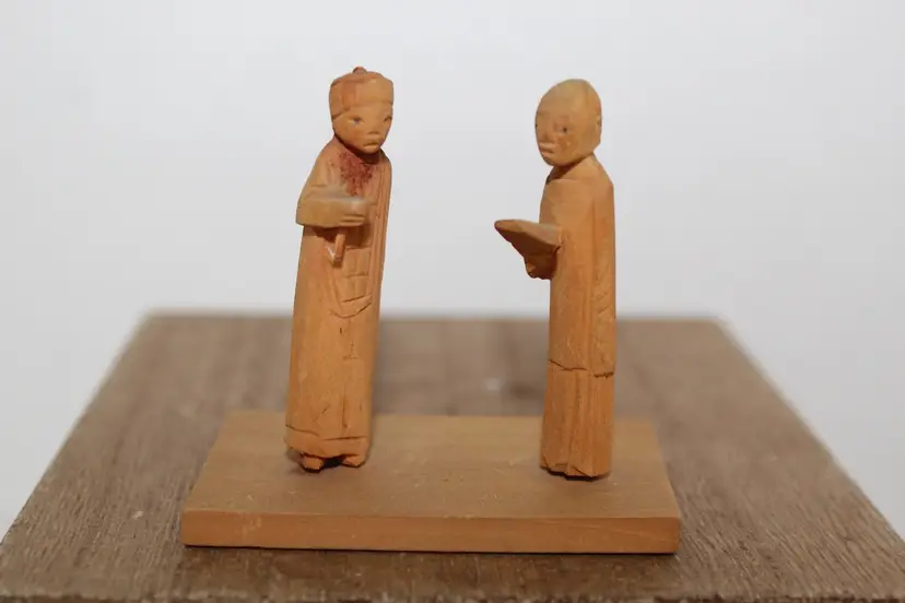 Two hand-carved wooden folk art figures in traditional attire on base