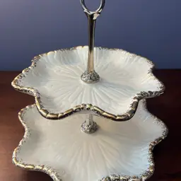 Mid-century two-tier ceramic serving tray Cream with gold trim. Silver Handle 10.5” Tall 
First Tier 9 Inches Across 
Second Tier 11 Inches Across
