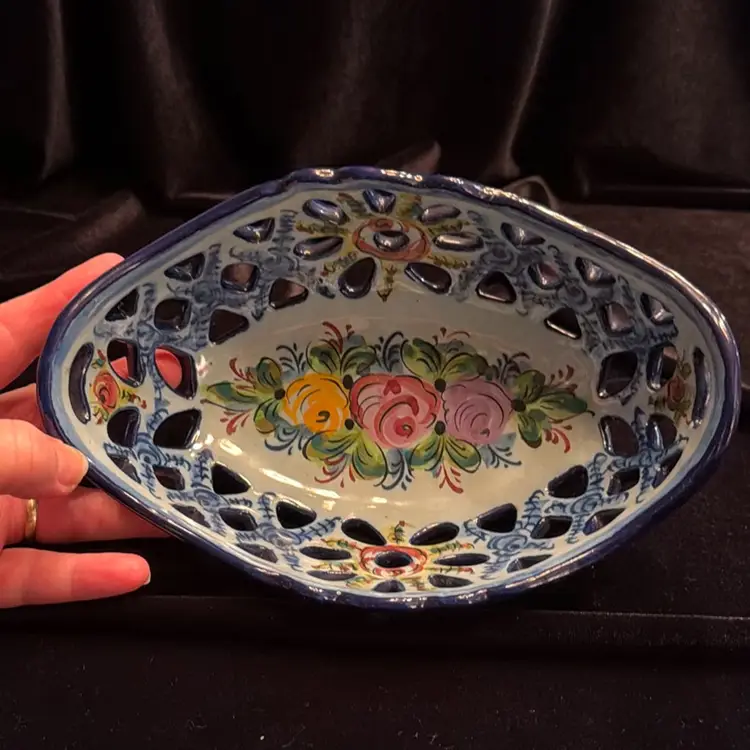 A vintage reticulated pottery centerpiece basket or bread bowl, manufactured in Alcobaça, Portugal. Hand-painted ceramic with a white glazed finish, blue trim, and colorful pink and yellow floral motifs.