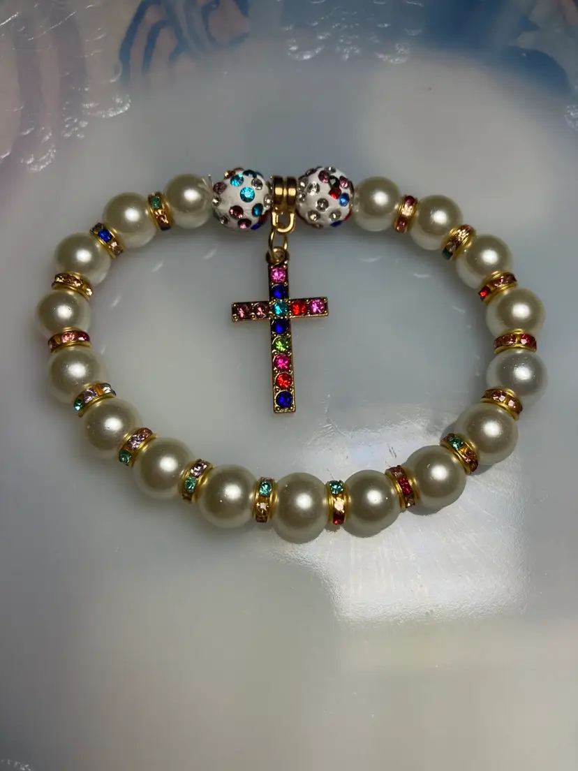 Cross and Faux Pearl Bracelet.
Multicolored Crystal Spacer Beads.
Multicolored Crystals in The Cross.
Gold Toned Accents. 
Stretch