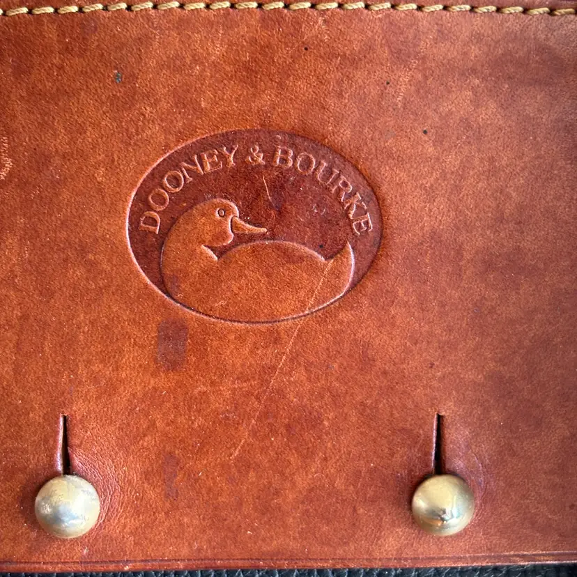 Dooney & Bourke Black & Tan Leather Handbag

Classic Dooney & Bourke handbag with pebbled leather. Tan leather trim and handles. Has a top zipper closure. Original Dooney & Bourke tag attached. Brass hardware is present. 

One stud detached from bag that isn’t noticeable (pictured)

Inside fabric needs cleaning