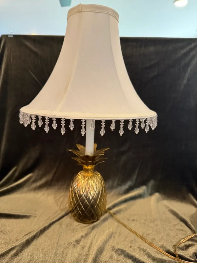 Beautiful, 
Hollywood Regency style accent lamp featuring a polished brass pineapple-shaped base and a white bell shade adorned with clear bead fringe.