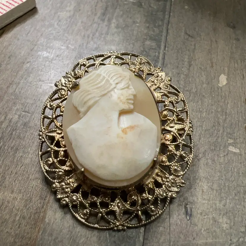 A hand-carved shell cameo brooch with a gold-toned filigree frame. 1890-1910