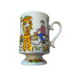 This is a vintage 1960s mod kitsch ceramic pedestal footed coffee mug with a "Boy Meets Girl" theme. 
The mug features psychedelic pop art illustrations of a girl holding an umbrella and a boy on a bicycle