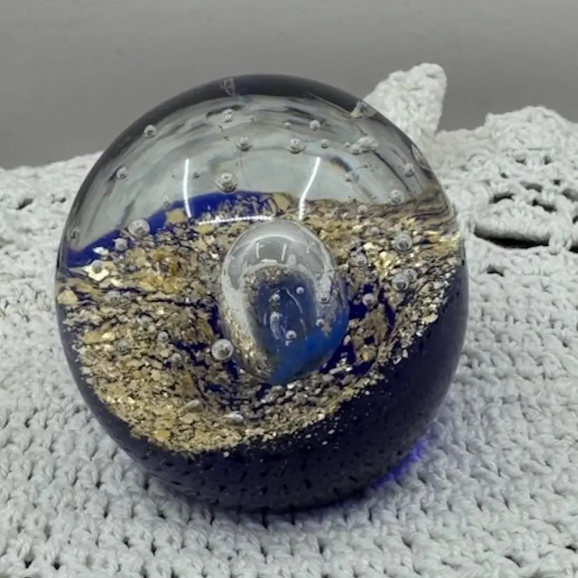 Handmade glass paperweight with blue, gold, and bubble inclusions, 2.5”