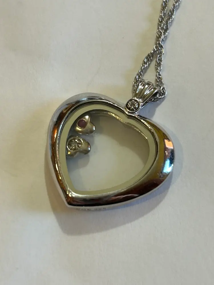 Bradford Gold Exchange (BGE) 925 Heart Shaped Locket
with two small heart-shaped trinkets free floating inside. Each have a stone centered in side. Small diamond on the top of the heart. Engraved with “ A MOTHER HOLDS HER CHILDREN’S HEARTS FOREVER.” Around the top edge which I think is the back of the necklace. This is on a very delicate 10 inch chain. Super super pretty necklace. Gems tested with presidium gem tester II.