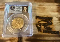 2007-P John Adams Presidential Dollar coin, graded MS66 by PCGS (Professional Coin Grading Service). This particular coin is designated as a "First Day of Issue - Position B