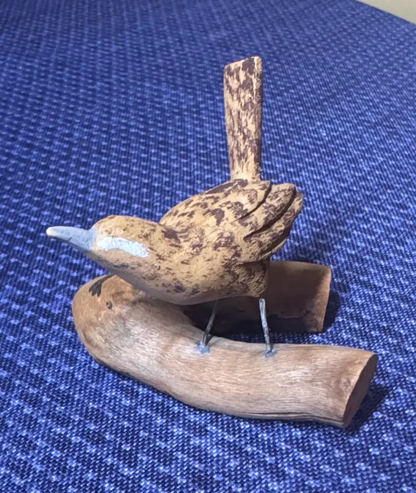 Hand carved wooden bird sculpture perched on a piece of natural wood signed