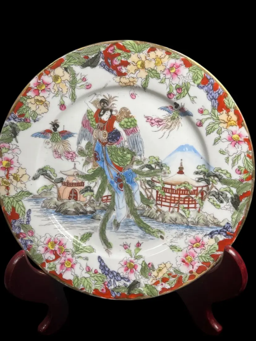 #01 Antique Nippon Porcelain Plate-Hand Painted Design w/ Vibrant Colors & Intricate Details. Beautiful Floral Border. Central Scene is a Woman w/ Wings-Similar to a Rising Phoenix-2 Other Figures on Her R & L. Gold Paint on Rim Used for Accent. Lot 48