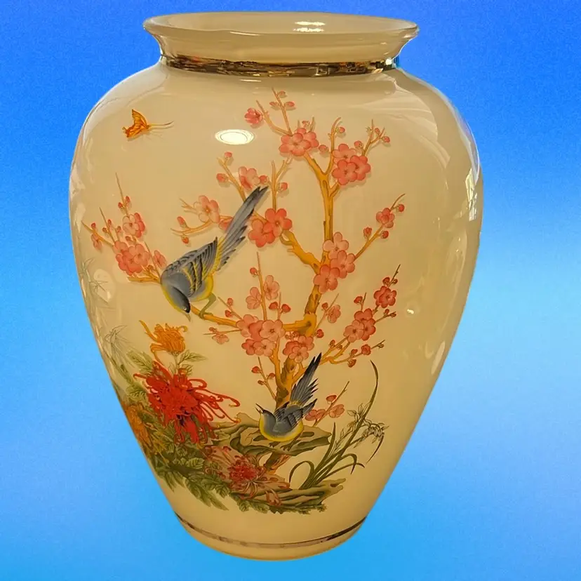 This Vintage Asian-style Cream Color On White Cased Glass Vase features a beautiful blue bird design with cherry blossoms and a butterfly, all glass with gold trim. The vase measures 9 1/2" in height and 6 1/2" in width,