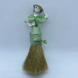 A vintage porcelain half-doll crumb brush with a straw bristle base.