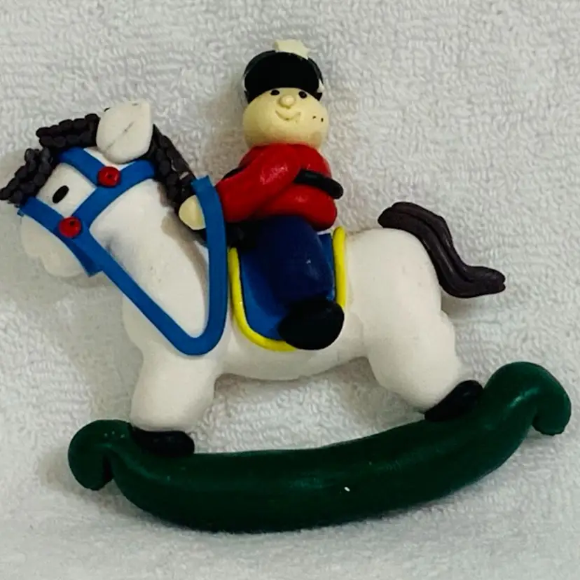 Unique Soft Acrylic Christmas Soldier On A Rocking Horse Ornament Cat Wearing A Red Jacket And Blue Trousers And A Black Uniform Hat With A White Star Detail Approximately 3.25” Tall And 4” In Length