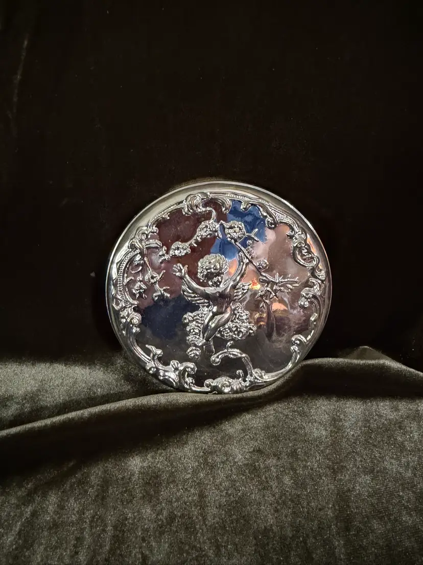 Ornate silverplate hand mirror with cherub and floral motifs.