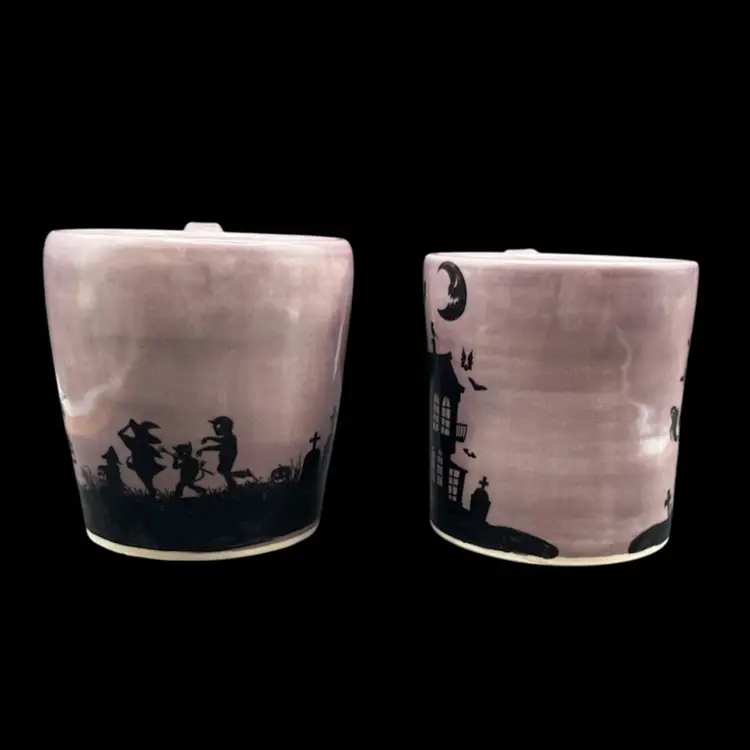 #217B Pair Of Halloween Themed Hand Made Pottery Mugs. Haunted House, Witches, Trick Or Treaters Smoky Purple With Black Silhouette  Scenes Around Both. 
Pottery By Debbie Stamped On Bottom.