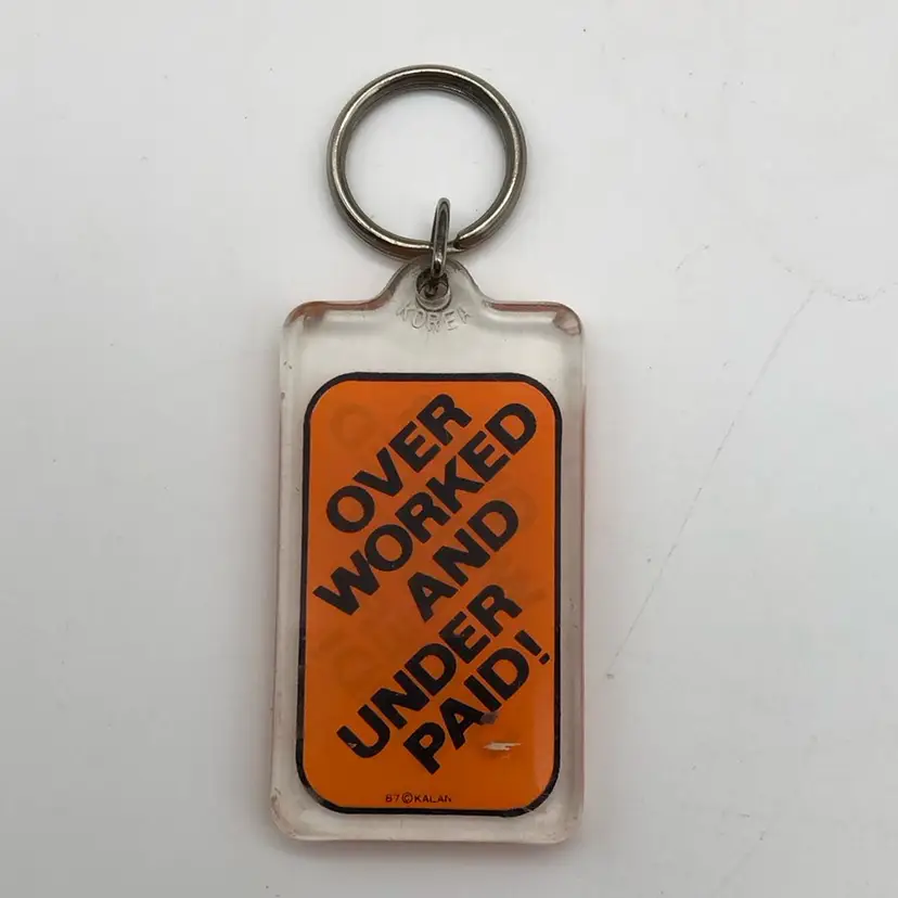 1987 Kalan Plastic Keychain says Over Worked And Under Paid!  3.5” x 1.5" includes ring