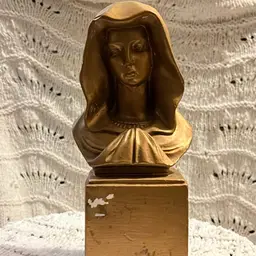 A bust of the Virgin Mary. This statue, often referred to as a Madonna bust, Is Gold In Color.
