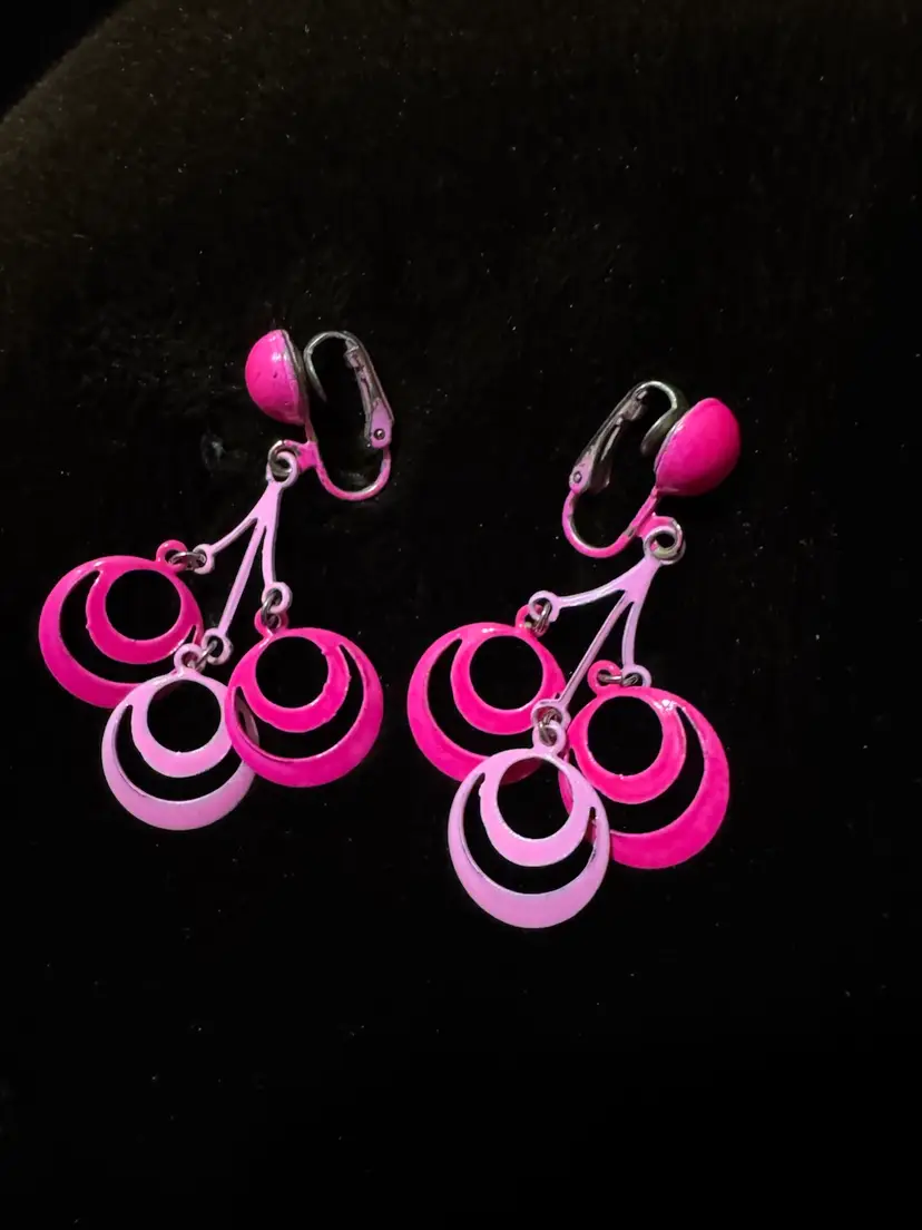 Pink clip-on dangle earrings feature a cascading geometric design of concentric circles