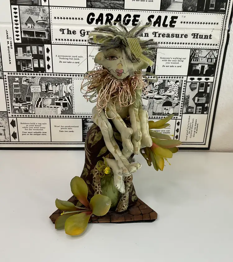 Forest Witch made of green and brown fabric, ribbon, silk flowers sitting on her house, hand painted face. Signed and dated 2004, 9” tall and 5 1/2” across base