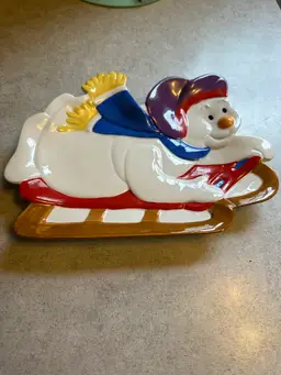 Ceramic decorative plate featuring a snowman on a sled.
