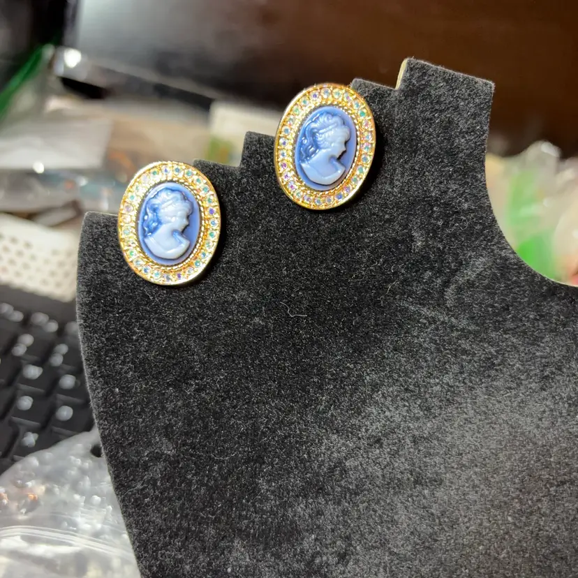 These earrings showcase a timeless blue and white cameo silhouette encircled by a radiant halo of sparkling rhinestones, crafted in a yellow gold-tone metal.