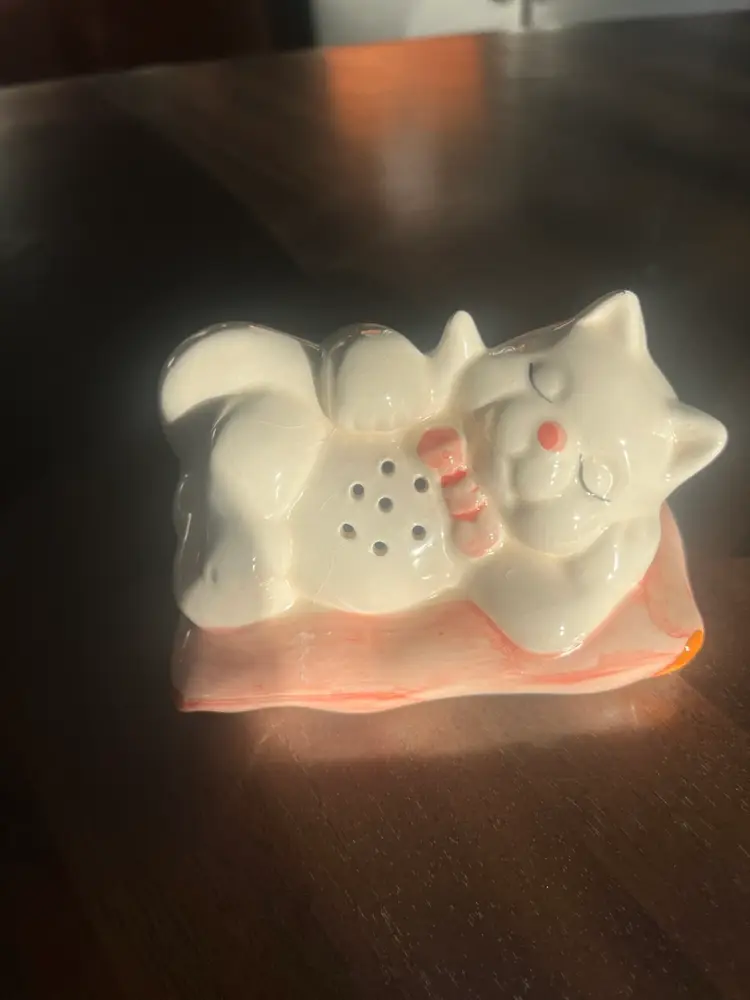This is a vintage Interpur ceramic sleeping cat shaker with a pink bow. 5”x3”