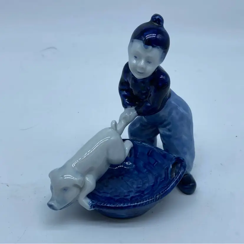 #1446 Delft-style porcelain figurine of a boy with a pig in a basket.