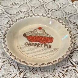 The Vintage Cherry Pie Plate Baking Dish is a charming addition to any kitchen collection, featuring a round ceramic piece with a colorful cherry pie design. This unique pie dish includes a cherry pie recipe, with its 10 1/4”diameter and 1.5" depth, this original piece from the 1980s is A Great nostalgic piece.  There is some crazing and a Small chip on the back shown in pictures.