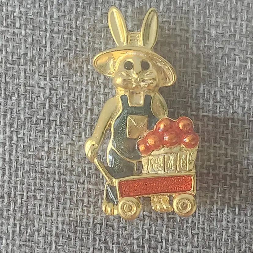 This is a Vintage Danecraft Farmer Bunny Pin Brooch, featuring a gold-tone rabbit wearing coveralls and pulling a wagon filled with fruit.