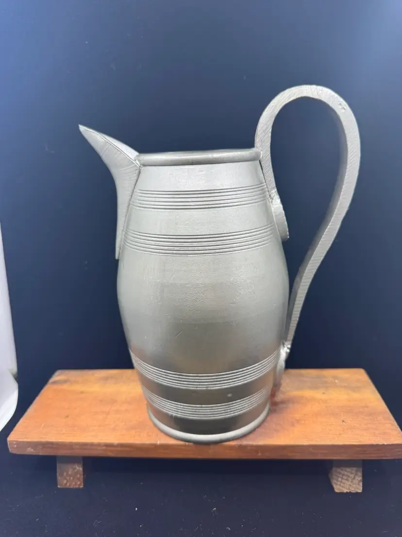 A vintage banded pewter(?) syrup pitcher with a curved handle, 8.5”